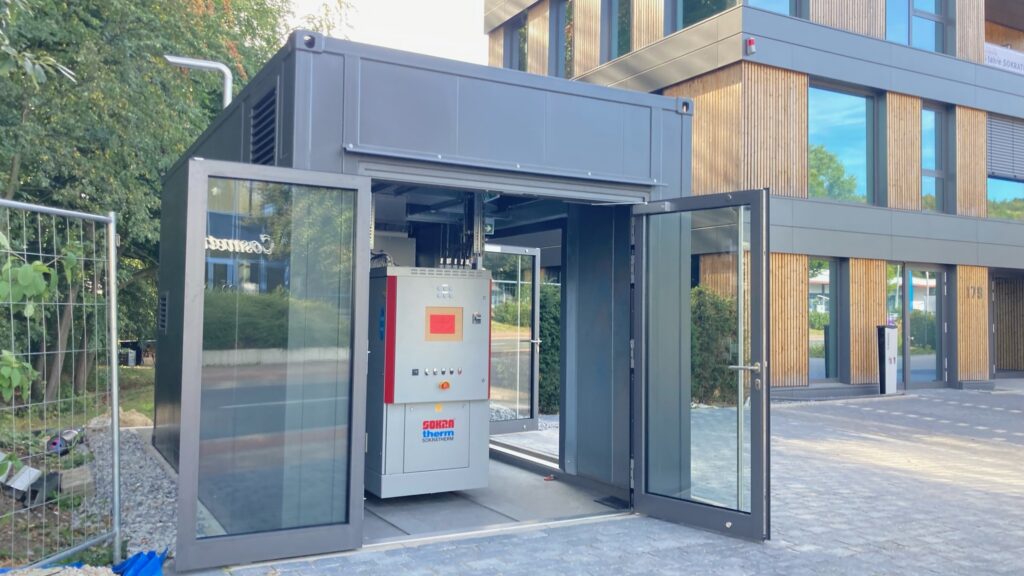 Sondercontainer mit Glastüren, in dem ein Blockheizkraftwerk ausgestellt ist